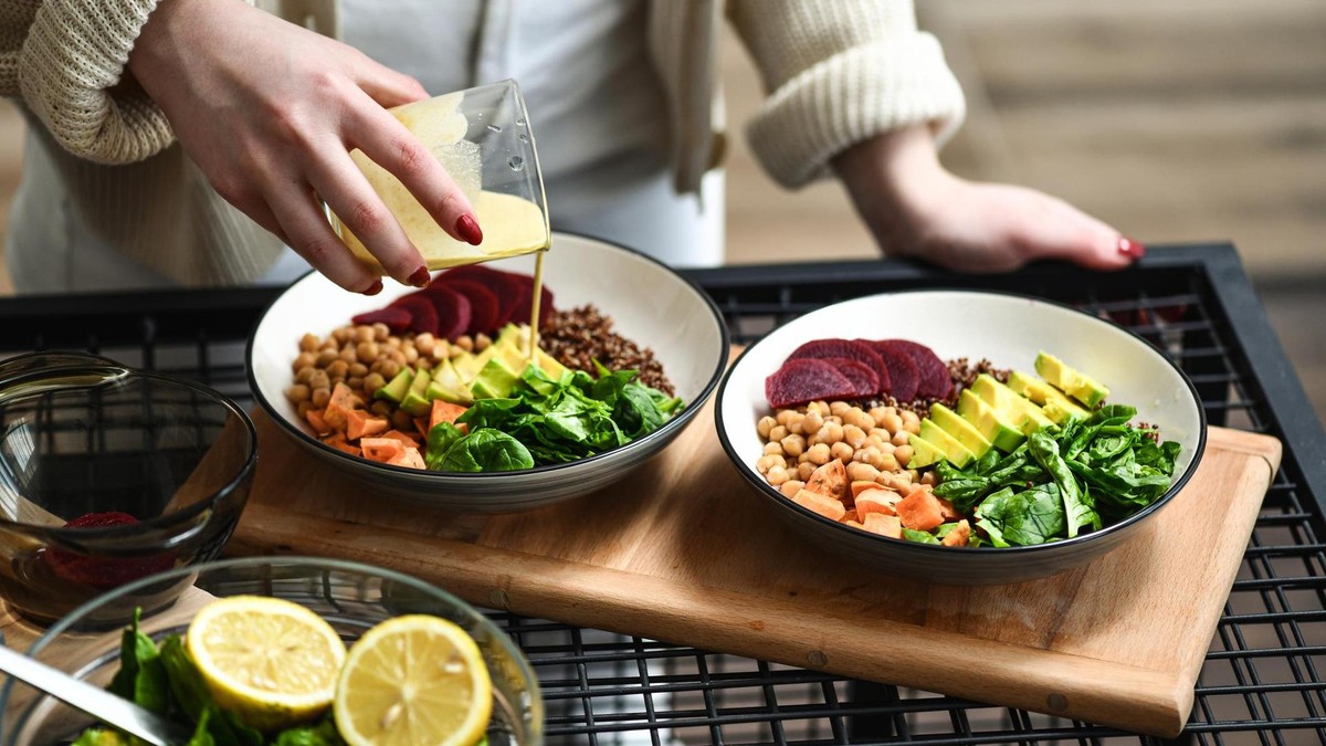 Eine Frau träufelt Dressing auf zwei Salat-Bowls 