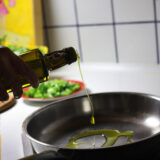 Eine Frau gibt beim Kochen Olivenöl in eine Pfanne.