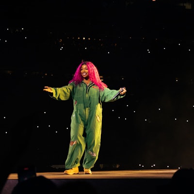 SZA steht links im grünen Overall auf dem Laufsteg im Stadioninnenraum, Kendrick Lamar rappt, von der Kamera abgewandt, rechts im Bild.