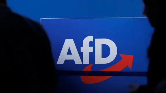 Der Schrifzug der AfD auf blauem Hintergrund mit schwarzen Schatten im Vorergrund. | Carsten Koall/dpa Der Schrifzug der AfD auf blauem Hintergrund mit schwarzen Schatten im Vorergrund.