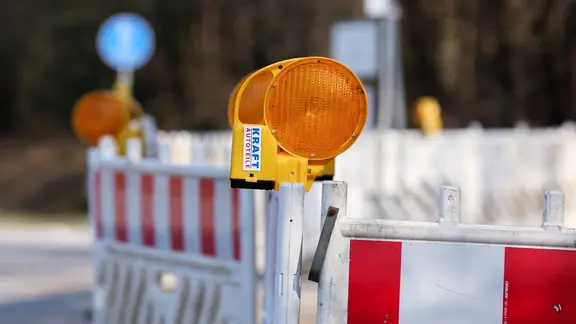 Für die Leitungsbauarbeiten und den Straßenbau erarbeitet die Stadt gerade einen Zeitplan. (Themenbild) | NDR, Pavel Stoyan Auf einer Straße stehen mehrere Baustellenzäune, an denen gelbe Baustellenlampen angebracht sind.