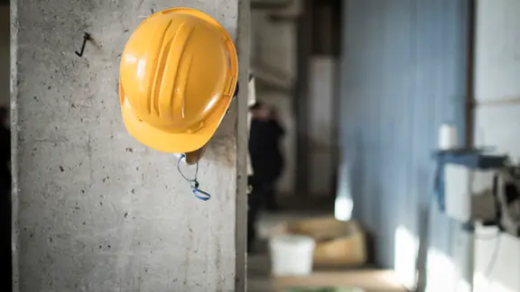 Ein Schutzhelm hängt an einer Säule auf einer Baustelle. | picture alliance, Florian Gaertner Ein Schutzhelm hängt an einer Säule auf einer Baustelle.