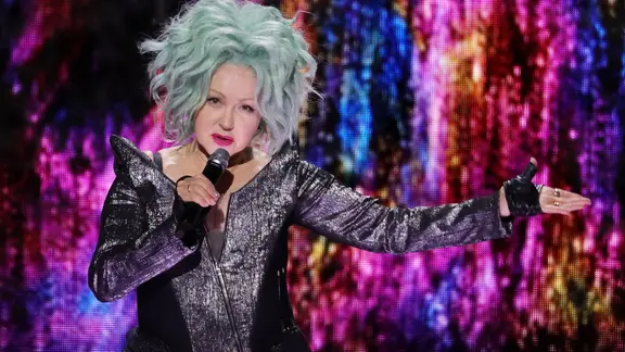 Cyndi Lauper steht mit hellblauen Haaren und einem Mikro auf der Bühne | picture alliance / Photoshot Cyndi Lauper steht mit hellblauen Haaren und einem Mikro auf der Bühne