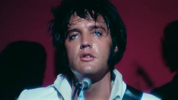 Szene aus "EPiC: Elvis Presley in Concert": Elvis Presley steht mit zerzausten Haaren und einem weißen Hemd vor einem Mikrofon
