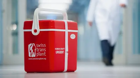 Rote Kühlbox mit Swiss Transplant-Logo in Krankenhausflur.