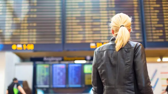Eine Frau steht vor einer Anzeigetafel an einem Flughafen. 