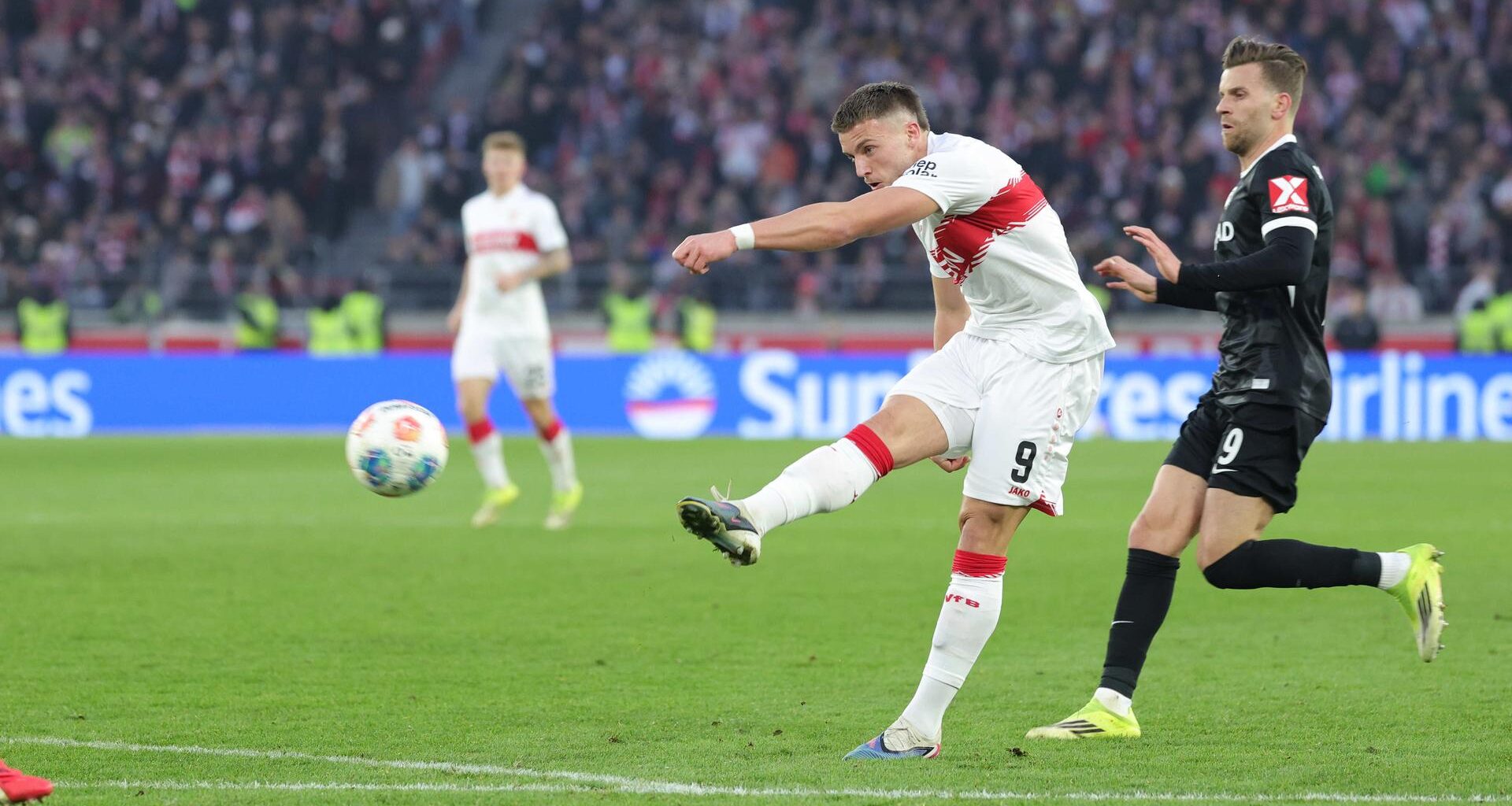 Ein Fußballer im weißen Trikot schießt mit dem Ball aufs Tor.