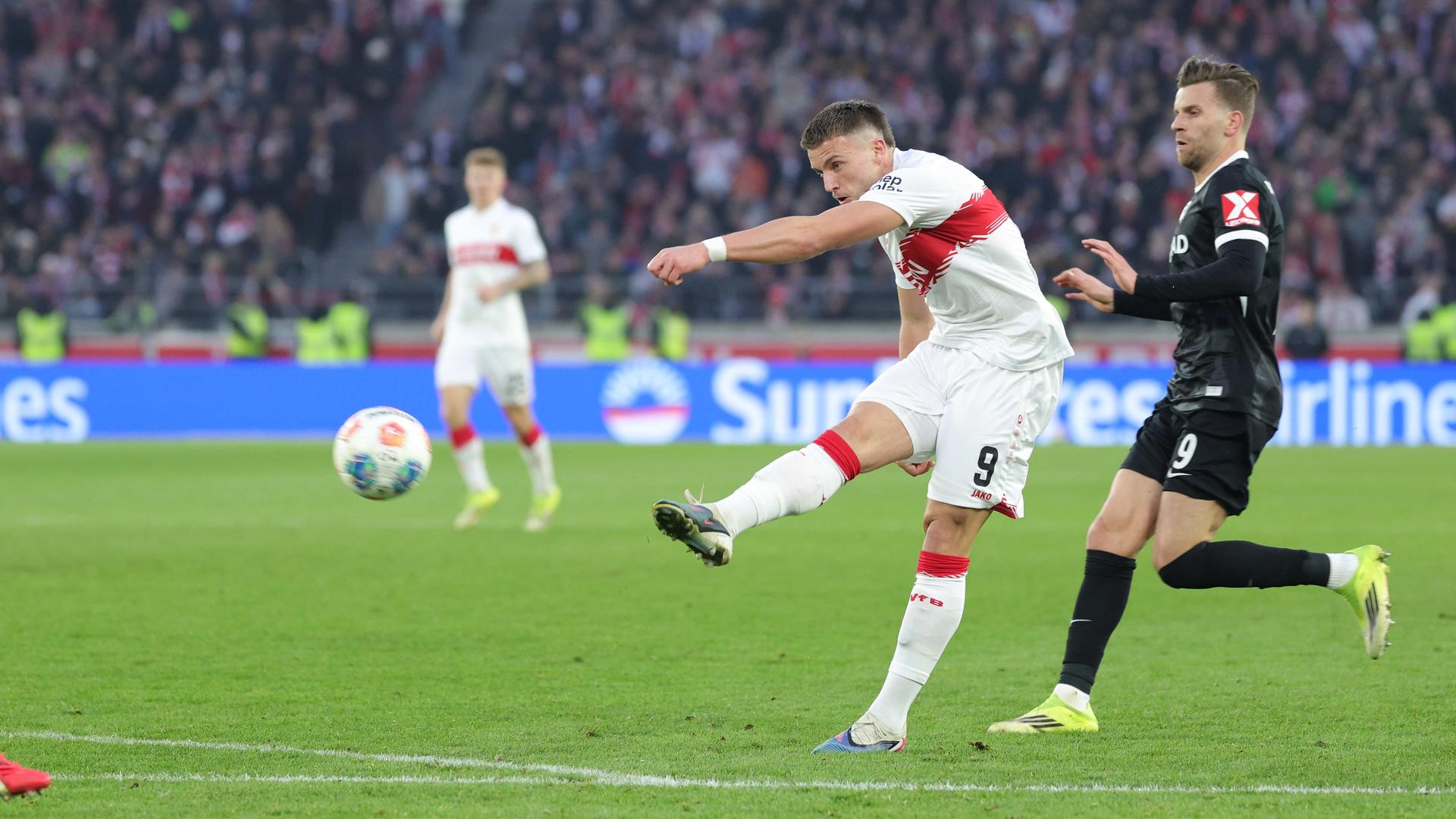 Ein Fußballer im weißen Trikot schießt mit dem Ball aufs Tor.
