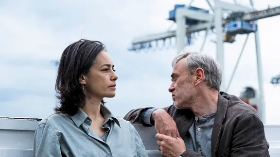 Szene aus dem Film "Gelbe Briefe": Eine Frau und ein Mann sitzen im Freien an einem Hafen | Ella Knorz ifProductions / Alamode Film Szene aus dem Film "Gelbe Briefe": Eine Frau und ein Mann sitzen im Freien an einem Hafen