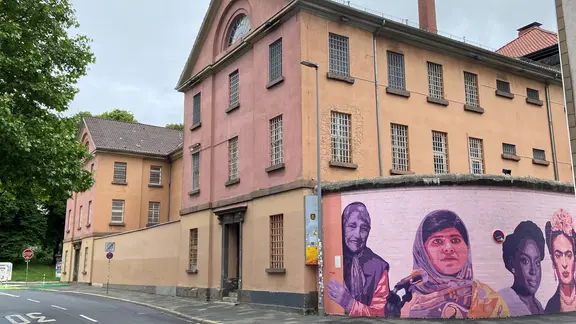 Das Bild zeigt die ehemalige JVA in der Göttinger Innenstadt. Auf einer Mauer sind übergroße Personen aufgemalt. | NDR/Bärbel Wiethoff, Bärbel Wiethoff Das Bild zeigt die ehemalige JVA in der Göttinger Innenstadt. Auf einer Mauer sind übergroße Personen aufgemalt.