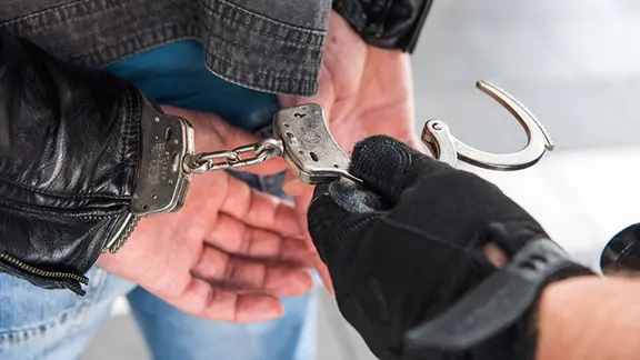 Ein Mann wird mithilfe von Handschellen festgenommen. (Symbolbild)