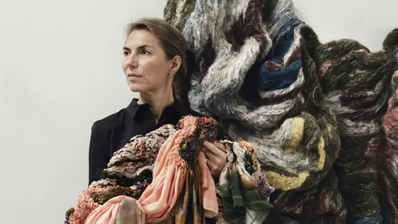 Ein Selbstporträt der Künstlerin Hanne Friis, eine Frau schaut zur Seite, über ihrer Schulter hängt ein großer bunter Stofffetzen.