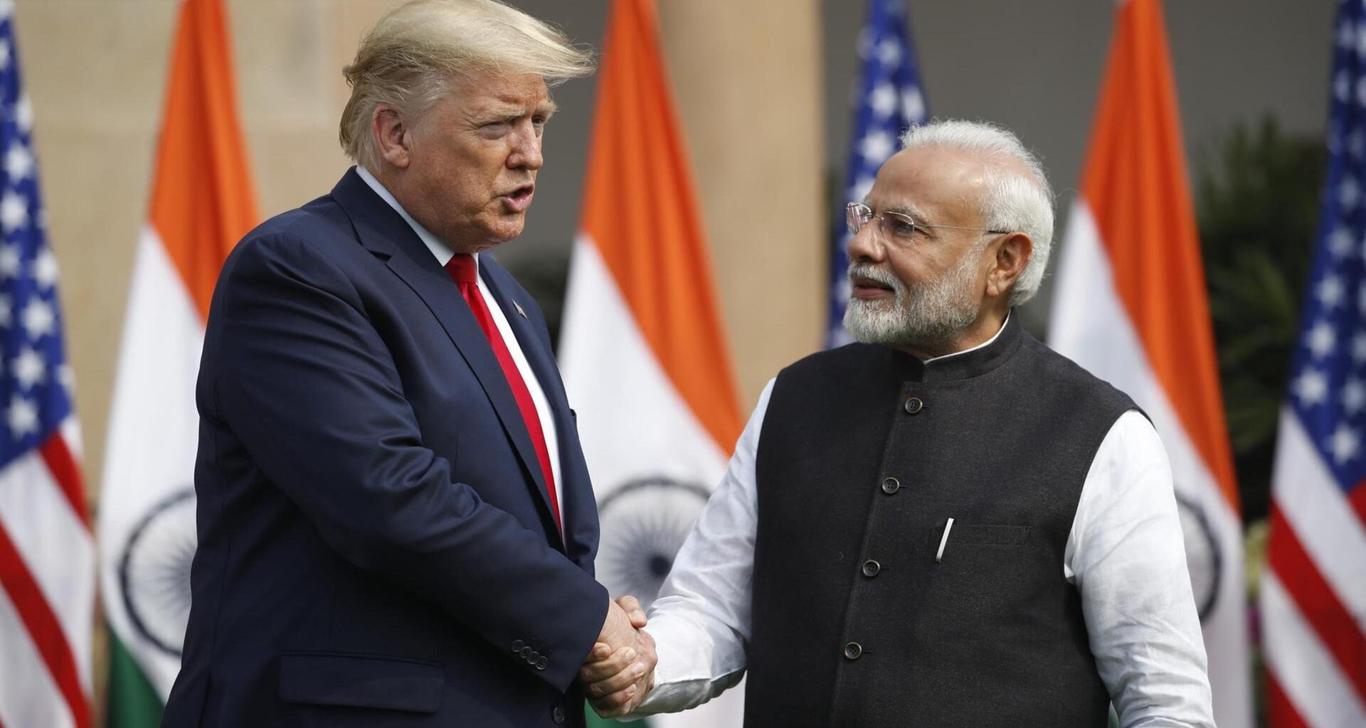 US-Präsident Trump schüttelt dem indischen Premierminister Modi die Hand. Ihnen ihnen die Flaggen der beiden Länder.