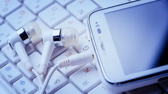 Kopfhörer mit Smartphone liegen auf einer Computertastatur. | Fotolia.com, Dmytro Titov Kopfhörer mit Smartphone liegen auf einer Computertastatur.