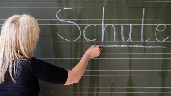 Eine Lehrerin schreibt das Wort "Schule" auf eine Schultafel in einem Klassenzimmer. | picture alliance / dpa, Axel Heimken Eine Lehrerin schreibt das Wort "Schule" auf eine Schultafel in einem Klassenzimmer.