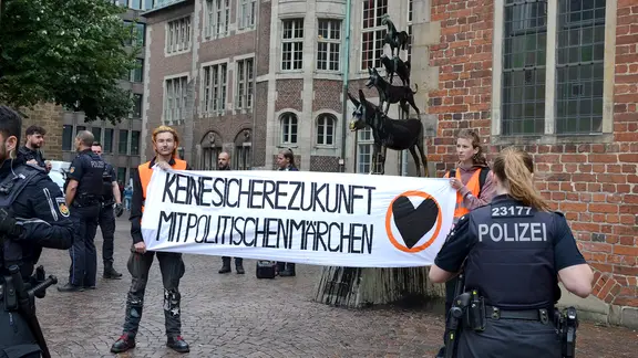 Aktivisten von "Letzte Generation" protestieren mit einem Plakat vor den Bremer Stadtmusikaten. Die Statue ist mit schwarzer Farbe beschmiert. | Letzte Generation Aktivisten von "Letzte Generation" protestieren mit einem Plakat vor den Bremer Stadtmusikaten. Die Statue ist mit schwarzer Farbe beschmiert.