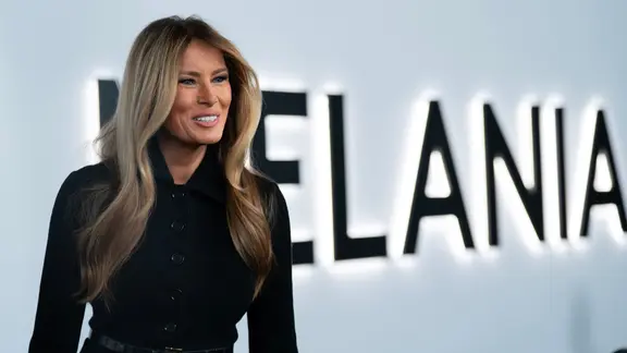 Melania Trump steht in einem schwarzen Mantel vor einer Wand mit großem Schriftzug "MELANIA". | picture alliance / ASSOCIATED PRESS | Jose Luis Magana Melania Trump steht in einem schwarzen Mantel vor einer Wand mit großem Schriftzug "MELANIA".