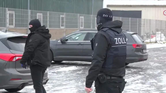 Zollbeamte stehen bei einer Razzia auf einem Firmengelände in Lübeck. | Nonstop News Zollbeamte stehen bei einer Razzia auf einem Firmengelände in Lübeck.