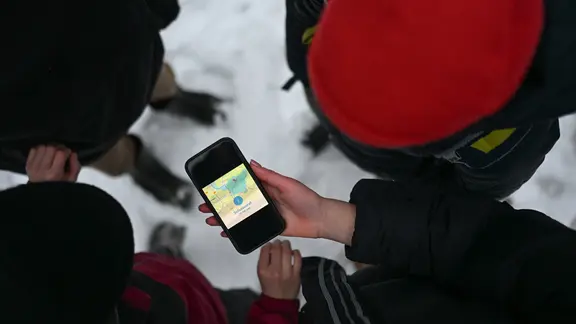 Vier Schüler blicken auf ein Smartphone, das den Schulausfall für den Landkreis Leer anzeigt.