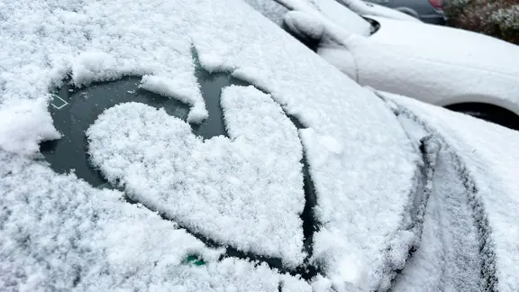 Ein Herz ist auf die schneebedeckte Windschutzscheibe eines Autos gemalt.