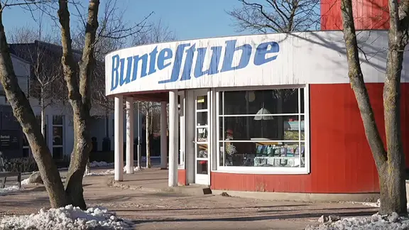 Die "Bunte Stube" in Ahrenshoop - mehr als nur ein Laden für Kunst und Bücher. | NDR.de Roter Laden mit weißem Dach und darauf mit blauer Schrift "Bunte Stube"