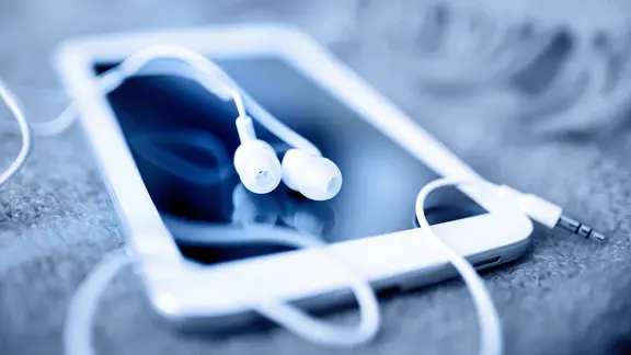 Ein Smartphone mit Kopfhörern liegt auf einer weichen Unterlage. | fotolia.com, maksim Ein Smartphone mit Kopfhörern liegt auf einer weichen Unterlage.
