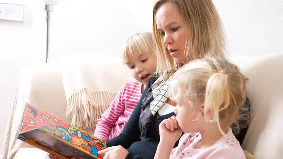 Beim gemeinsamen Lesen können Kinder in spannende Wintergeschichten eintauchen. | colourbox, - Mutter liest zwei Töchtern aus einem Kinderbuch vor.