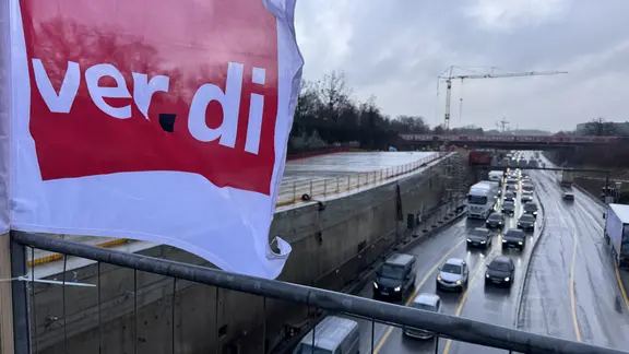 Eine ver.di-Fahne weht und im Hintergrund ist ein Stau zu sehen. | NDR Eine ver.di-Fahne weht und im Hintergrund ist ein Stau zu sehen.