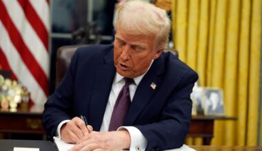 Donald Trump sitzt an einem Schreibtisch vor einer US-Fahne im Weißen Haus und unterzeichnet ein Dekret.