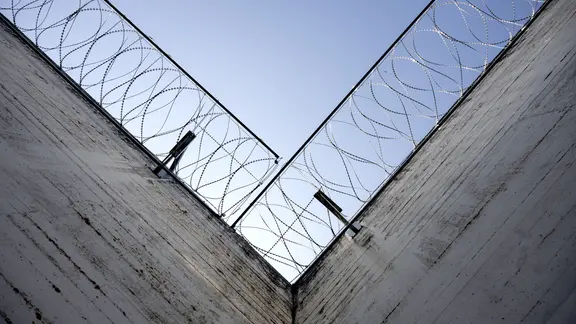 Stacheldraht säumt die Mauern in einem Gefängnis, der Blick geht an den Mauern entlang in den Himmel. | picture alliance/KEYSTONE | ENNIO LEANZA, ENNIO LEANZA Stacheldraht säumt die Mauern in einem Gefängnis, der Blick geht an den Mauern entlang in den Himmel.