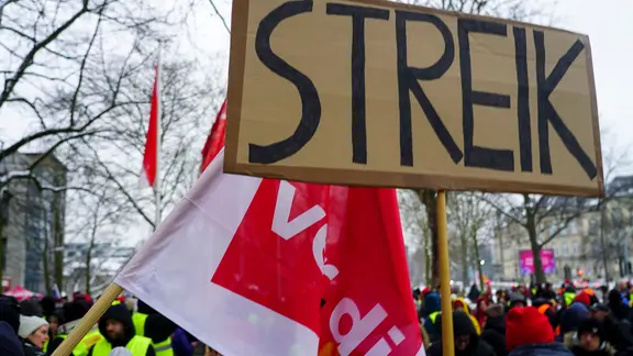 Ein Pappschild mit der Aufschrift "Streik" - daneben eine ver.di-Flagge.