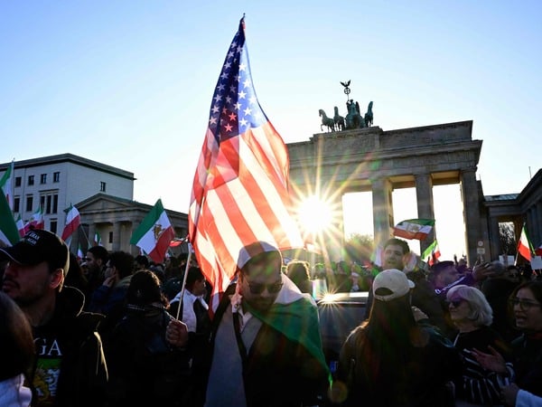 A man with a US flag attends a demonstration in front of the Brandenburger Gate in Berlin, on March 1, 2026. The United States and Israel launched strikes against Iran on February 28, sparking fears of regional war with explosions reported across the Middle East as the Islamic republic retaliated with barrages of missiles. (Photo by Tobias SCHWARZ / AFP)