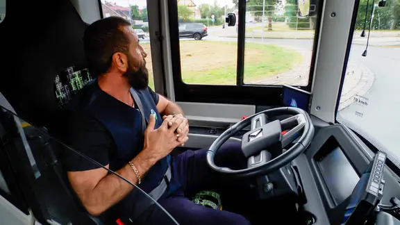 Ein Busfahrer sitzt in einem autonomen Bus hinter dem Lenkrad und faltet die Hände. | NDR Screenshot Ein Busfahrer sitzt in einem autonomen Bus hinter dem Lenkrad und faltet die Hände.