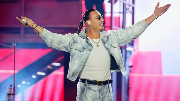 Der Rapper Apache 207 steht mit ausgebreiteten Armen während einer Show auf der Bühne und schaut zur Seite | picture alliance/dpa | Uwe Anspach Der Rapper Apache 207 steht mit ausgebreiteten Armen während einer Show auf der Bühne und schaut zur Seite