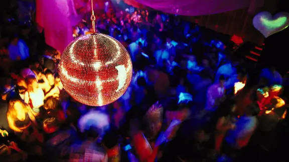 Eine Discokugel hängt in einem Club über tanzenden Menschen. | picture alliance Eine Discokugel hängt in einem Club über tanzenden Menschen.