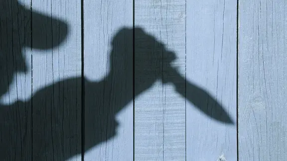Eine Silhouette eines Mannes mit einem Messer vor einer Holzwand. | fotolia.com, Alex Eine Silhouette eines Mannes mit einem Messer vor einer Holzwand.
