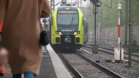 Menschen stehen am Bahngleis während ein Zug der Nordbahn fährt ein. | NDR Menschen stehen am Bahngleis während ein Zug der Nordbahn fährt ein.