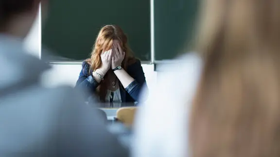 Eine Lehrerin hält sich resigniert die Hände vors Gesicht.