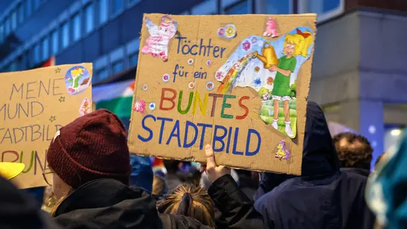 Eine Demonstrantin hält ein Schild mit der Aufschrift "Töchter für ein buntes Stadtbild" hoch. | picture alliance/dpa, Alex Talash Eine Demonstrantin hält ein Schild mit der Aufschrift "Töchter für ein buntes Stadtbild" hoch.