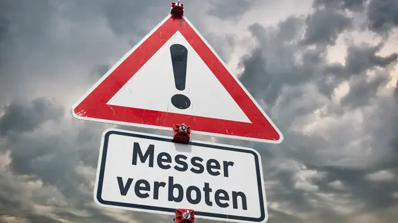 Warnschild "Gefahrstelle" und ein Zusatzschild mit der Aufschrift "Messer verboten" vor bewölktem Hintergrund. | picture alliance / SULUPRESS.DE | Torsten Sukrow / SULUPRESS.DE, Torsten Sukrow Warnschild "Gefahrstelle" und ein Zusatzschild mit der Aufschrift "Messer verboten" vor bewölktem Hintergrund.