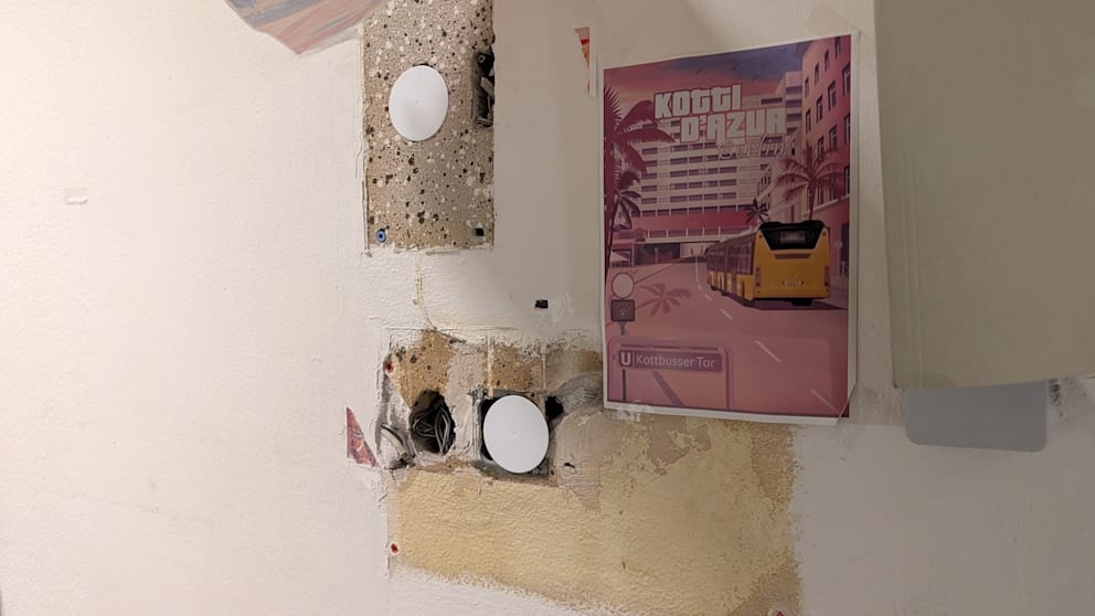 Ungefährlich sehen diese Löcher und Kabel in der Wand nicht aus – die Polizisten haben sie ironischerweise mit einem „Kotti D‘azur“-Poster verschönert