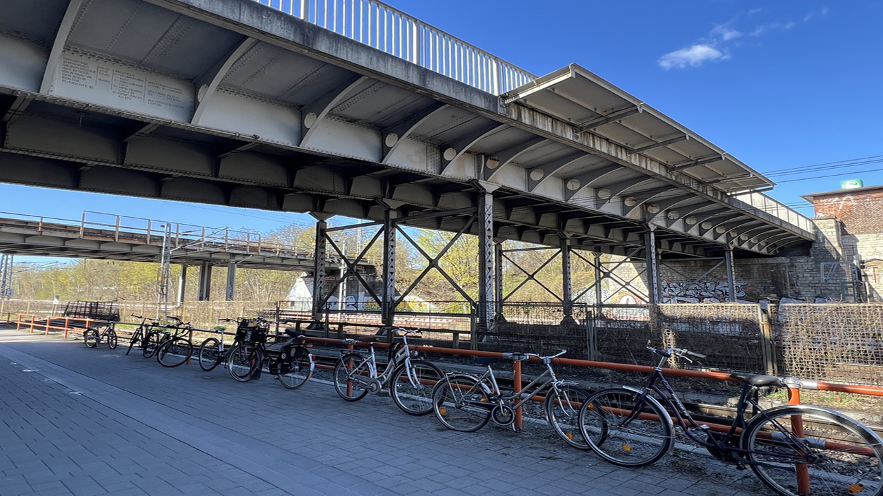 Die Köpenicker-Allee-Brücke an der Rudolf-Rühl-Allee in Köpenick ist seitlich zu sehen, mit Fahrrädern, Stahlstützen und dem angrenzenden Bahnhofsbereich.