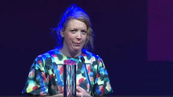 Eine Frau mit hochgesteckten Haaren hält eine Dankesrede für ihren Preis (Lina Beckmann im Ernst-Deutsch Theater) | Screenshot Eine Frau mit hochgesteckten Haaren hält eine Dankesrede für ihren Preis (Lina Beckmann im Ernst-Deutsch Theater)