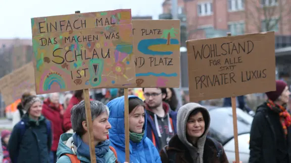 Menschen halten ihre Schilder auf einer Fridays for Future Demo.