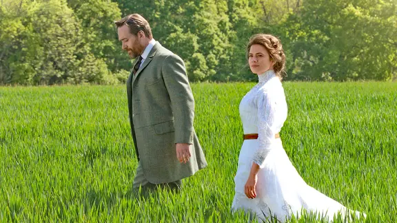 Henry Wilcox (Matthew Macfadyen, l.) und Margaret Schlegel (Hayley Atwell, r.) | © WDR/2017 Starz Entertainment, LLC, Ein Mann und eine Frau gehen durch hohes grünes Gras.
