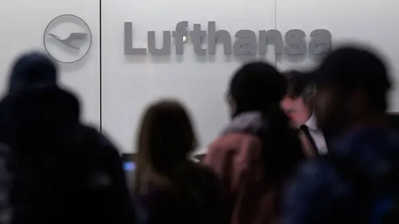 Menschen stehen vor einem Lufthansa-Schalter am Flughafen.
