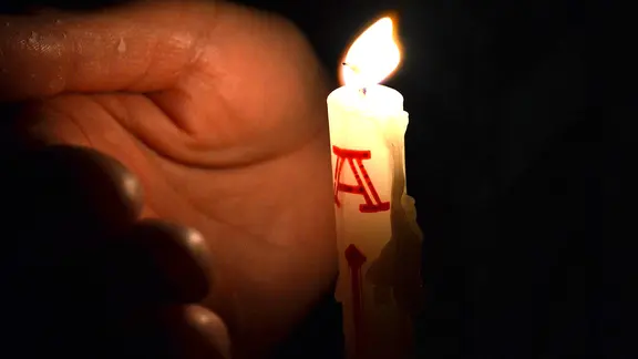 Eine Osterkerze leuchtet eine Hand an.