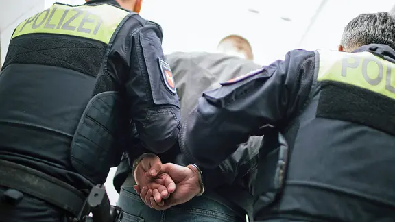 Zwei Einsatzkräfte der Polizei führen einen Mann mit angelegten Handschellen ab. | NDR, Julius Matuschik Zwei Einsatzkräfte der Polizei führen einen Mann mit angelegten Handschellen ab.