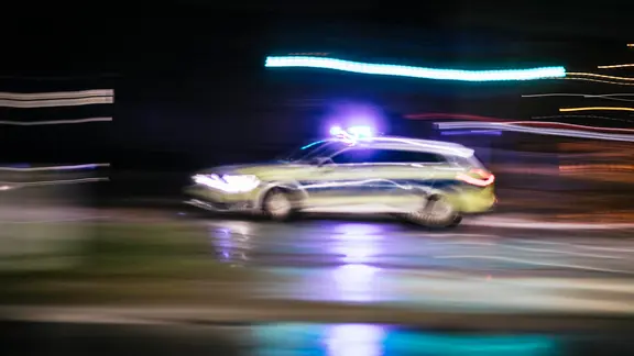 Ein Streifenwagen fährt bei Dunkelheit mit eingeschaltetem Blaulicht.