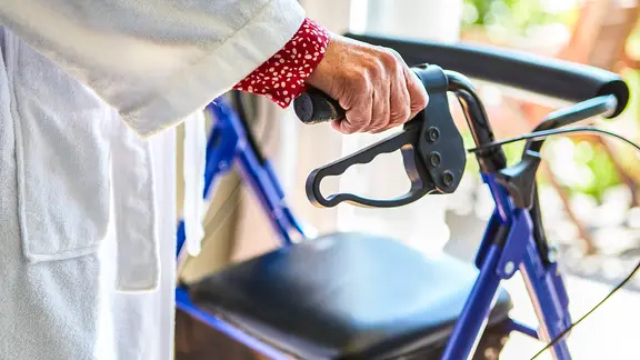 Eine Seniorin im Bademantel hält sich an einem Rollator fest. | picture alliance/Zoonar, Robert Kneschke Eine Seniorin im Bademantel hält sich an einem Rollator fest.